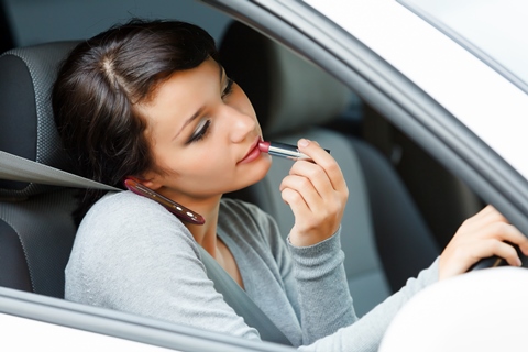 Female driver talking by mobile telephone and doing make-up.